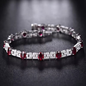 A bracelet featuring a series of oval-cut ruby stones alternated with round-cut diamonds, set in a solid 18k white gold band.
