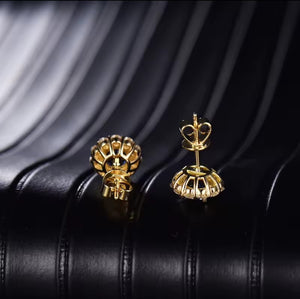 A pair of gold crown stud sapphire earrings shown from the back, resting on a black textured leather surface.