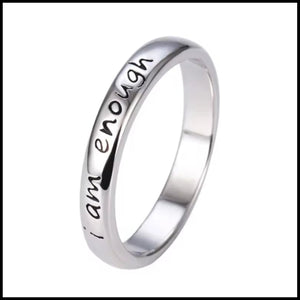 Silver band ring engraved with "I am enough" affirmation on a polished surface