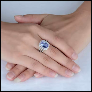 Close-up of a hand wearing a diamond ring with a blue gemstone on a light background