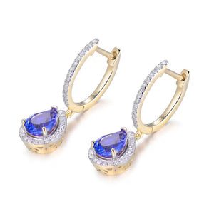 A pair of gold huggie hoop earrings with a teardrop-shaped blue tanzanite centre stone, surrounded by a halo of small clear natural diamond stones, set against a plain white background.