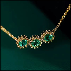 Gold necklace with emerald green gemstones on a dark green background