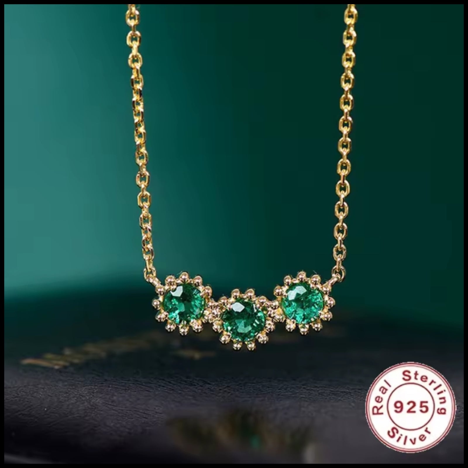 Gold necklace with green gemstones on a dark background, featuring 'Real Sterling Silver' certification.