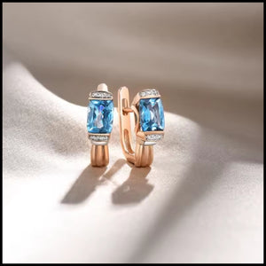 Rose gold hoop earrings with blue gemstones on a beige background
