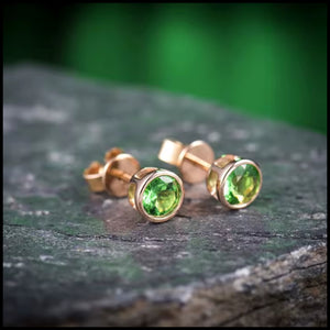 Tsavorite green stud earrings with round-cut gemstones set in 14k rose gold on stone surface