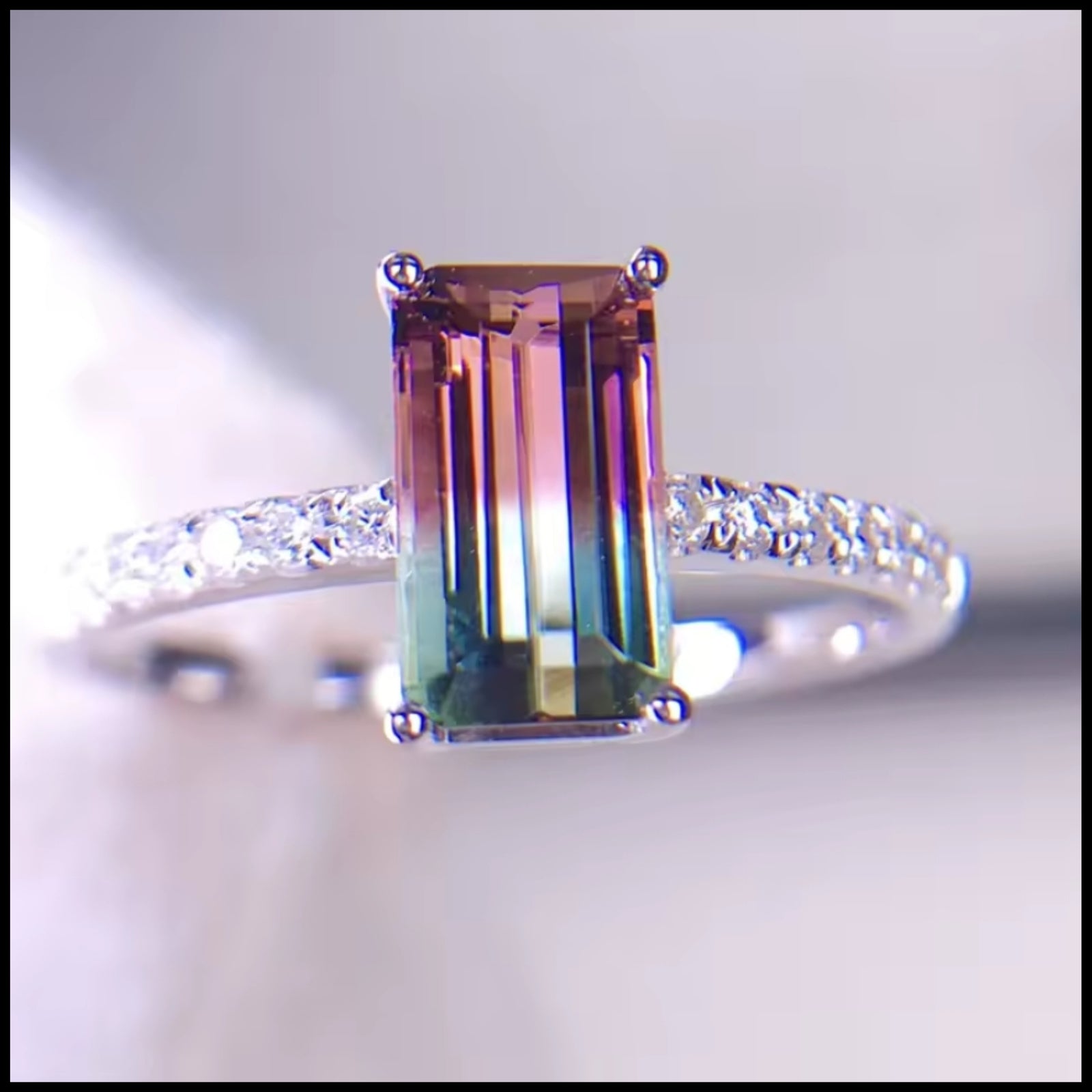 Ring with a green gemstone and diamond-studded band on a light gray background