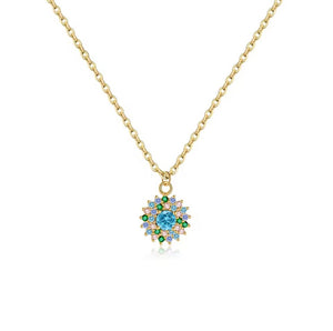 A gold chain necklace with a circular pendant featuring a light blue center stone surrounded by small green and clear stones, shown on a white background.