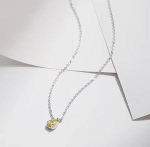 A delicate silver chain necklace with a small pear-shaped yellow cz gemstone pendant, displayed on a clean white background with soft shadows.