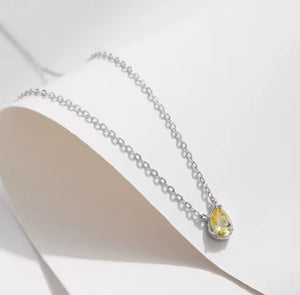 A silver chain necklace with a teardrop-shaped yellow gemstone pendant, displayed on a white curved jewelry bust against a clean white background.