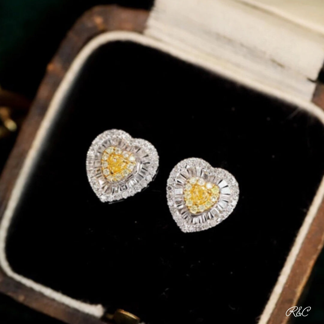 A pair of heart-shaped yellow diamond earrings in a case, with a white gold band connecting the hearts.