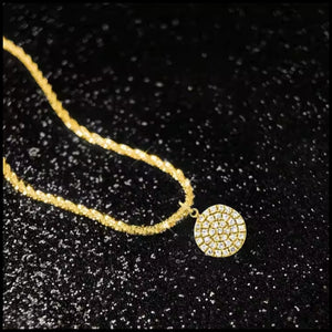 Gold necklace with a round, beaded pendant on a black textured background