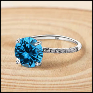 A solid silver ring with a blue zirconia center stone, set with smaller zirconia stones along the band.