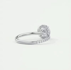 A silver moissanite ring with a halo-style setting and a pave band, shown from a side angle on a light grey background.
