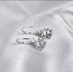A pair of diamond drop earrings with textured, flower-like circular charms, displayed on a soft, light grey satin fabric background.
