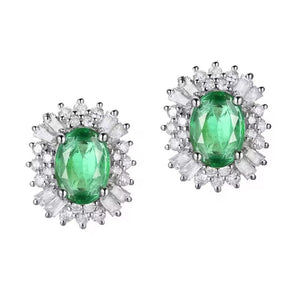 A pair of oval emerald green gemstone stud earrings surrounded by clear baguette and round-cut diamond stones in a white gold setting, shown on a plain white background.