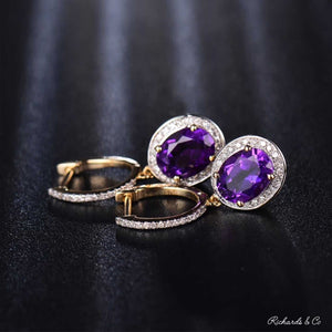 Elegant purple amethyst and diamond drop earrings set in 14k yellow gold with oval amethyst stones surrounded by sparkling diamonds