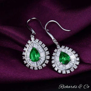 Clarity Drop Emerald & Diamond Earrings 18k white gold pear-cut emeralds surrounded by baguette and round diamonds on purple fabric