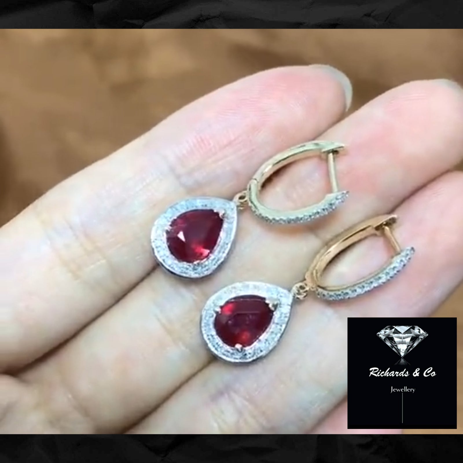A pair of ruby and diamond earrings held in a person's hand, with the brand name 'Richards & Co. Jewellery' visible.