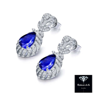 Tanzanite and diamond drop earrings set in 14K white gold with pear-cut blue tanzanite and round radiant diamonds