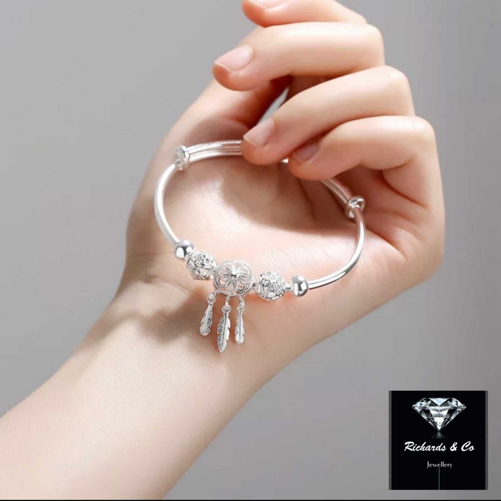 Hand holding a stylish solid silver dream catcher bracelet bangle with detailed charms