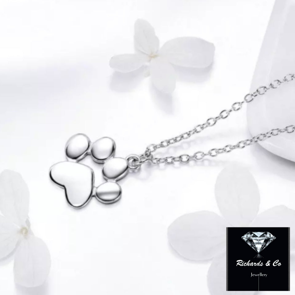 Sterling silver paw print necklace pendant on a delicate link chain surrounded by white flowers